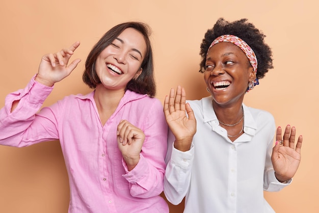 Photo gratuite de magnifiques amies diverses dansent sans souci avec le rythme de la musique passent du temps ensemble à la fête ont de la bonne humeur isolée sur fond beige. concept d'émotions amusantes d'amitié de personnes