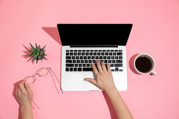 Main à l'aide d'un ordinateur portable sur une surface rose