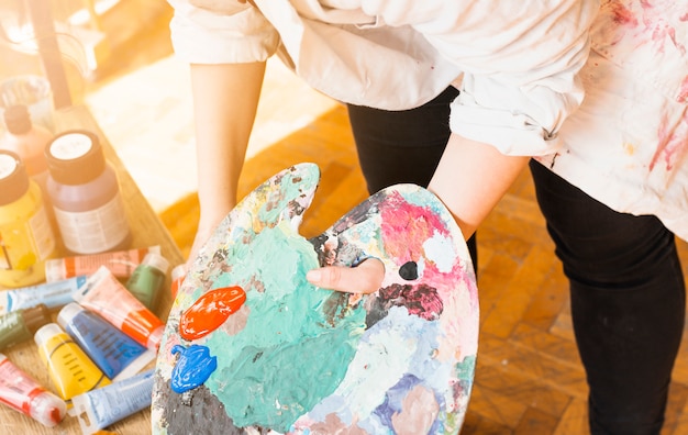 Main d&#39;artiste femme tenant une palette de peinture en désordre à l&#39;atelier