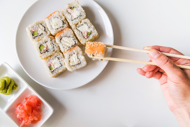 Main avec des baguettes saisissant un rouleau de sushi