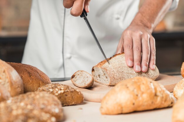Main de boulanger mâle coupant le pain avec un couteau tranchant