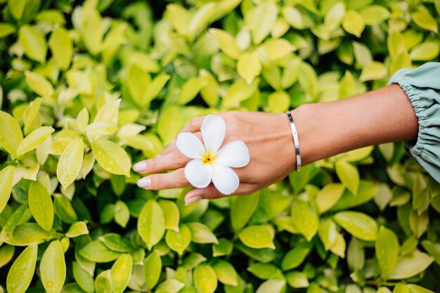 Main bronzée avec manucure naturelle avec un joli bracelet en argent avec une fleur blanche thaïlandaise plumeria