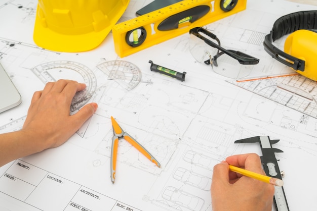 La main sur la construction des plans avec un casque jaune et outil de dessin