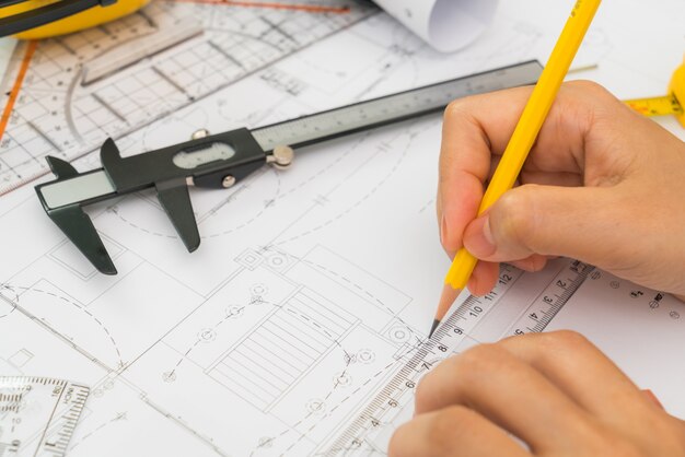 La main sur la construction des plans avec un casque jaune et outil de dessin