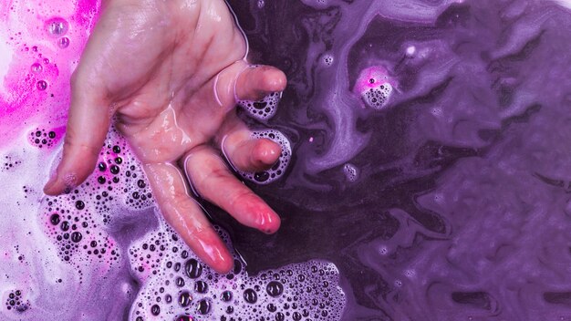La main dans un liquide violet avec mousse rose et blobs