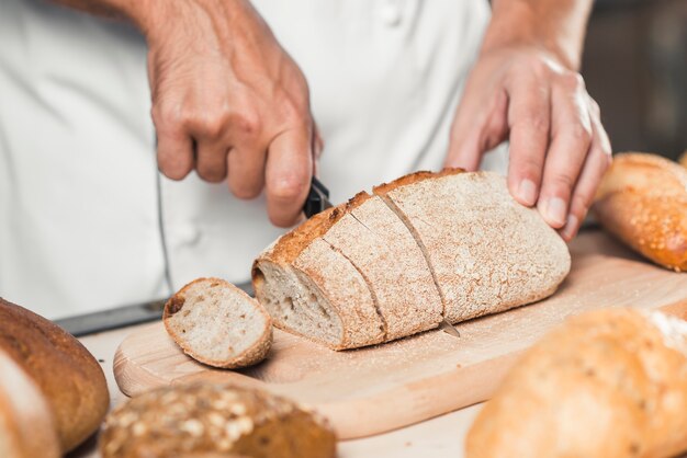 Main du boulanger coupant du pain frais avec un couteau