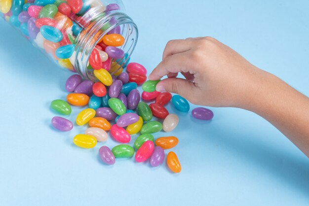 La main de l'enfant tenant plusieurs Jelly Beans sur une surface bleue