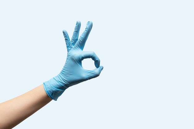 Main féminine dans des gants jetables sur fond bleu clair.