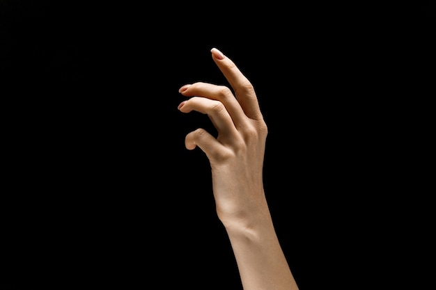 Main féminine démontrant un geste de toucher isolé sur fond noir de studio. Concept d'émotions humaines, de sentiments, de phycologie ou d'entreprise.