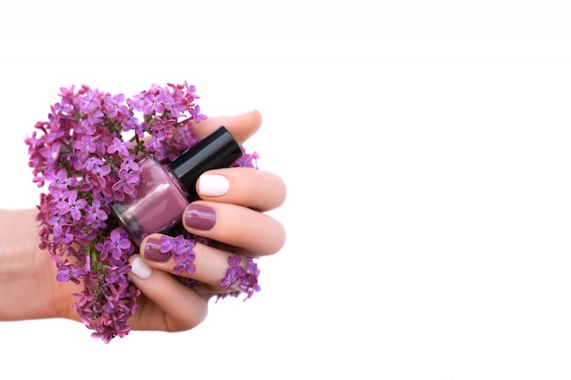 Main féminine avec des ongles blancs et violets tenant des fleurs lilas