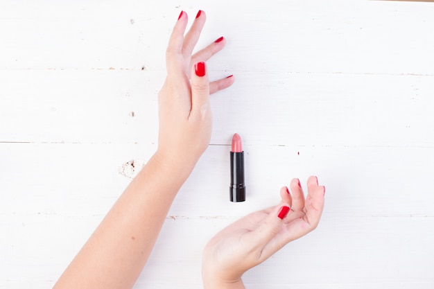 Main féminine avec des ongles rouges prenant le rouge à lèvres