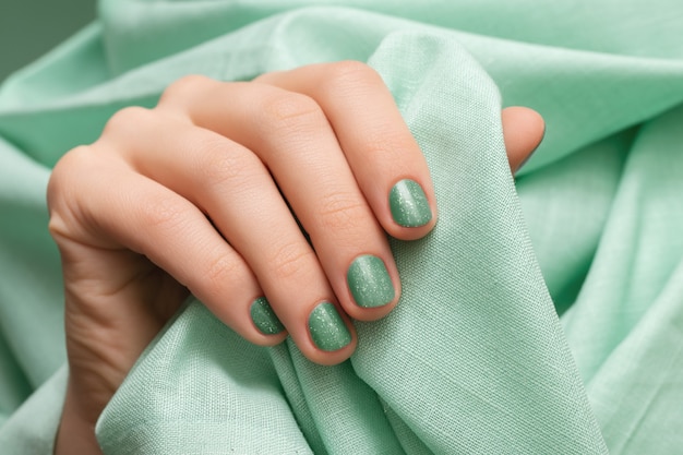 Main féminine avec des ongles verts scintillants