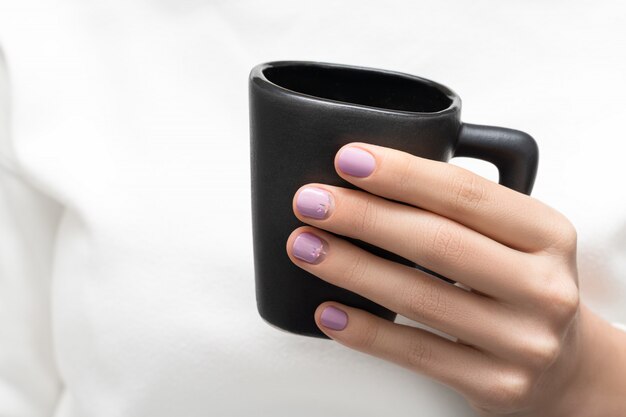 Main féminine avec des ongles violets tenant une tasse à café noire