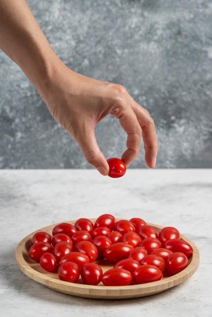 Main Féminine Prenant La Tomate De La Plaque En Bois.