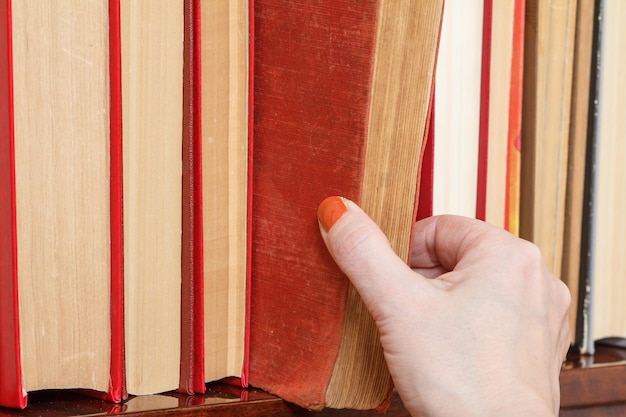 La main féminine prend un livre dans une étagère. de nombreux livres cartonnés sur étagère en bois. notion de bibliothèque