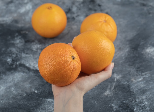 Main féminine tenant des oranges sur une table en marbre.