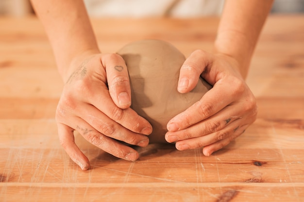 Main de femme malaxant l&#39;argile sur une table en bois