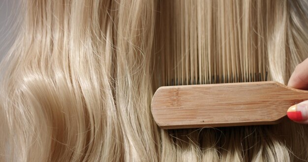 La main d'une femme avec une manucure brillante qui traverse de longs cheveux blonds ondulés