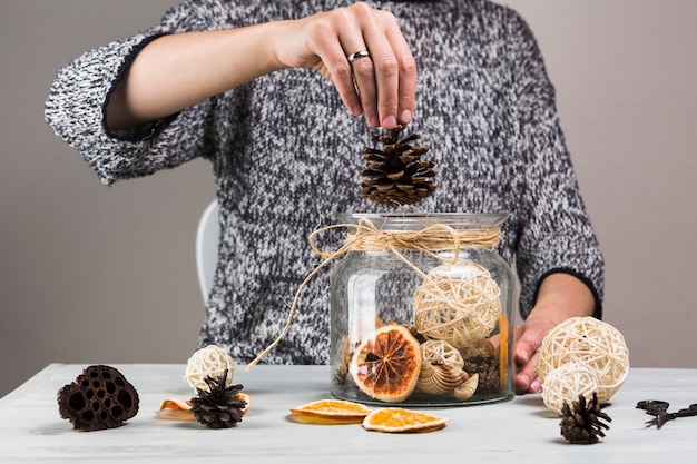 Photo gratuite main de femme mettant une pomme de pin dans un bocal en verre