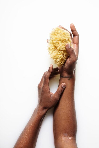 Main de femme noire dans un bain de lait avec une éponge jaune