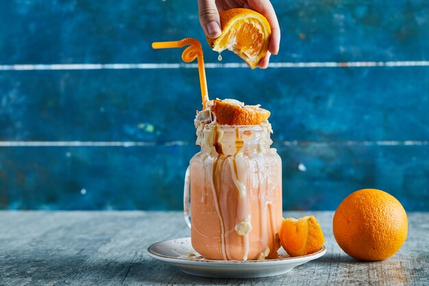 Une main de femme serrant une orange en smoothie et tranche d'orange sur plaque blanche