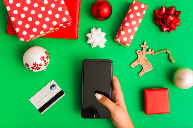 Main de femme avec smartphone près de carte en plastique et ensemble de décorations de Noël