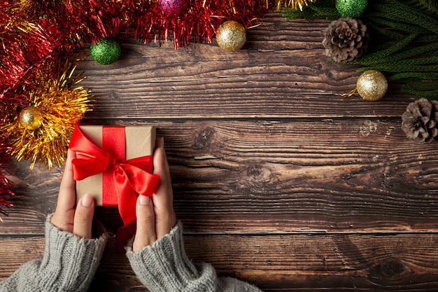 Main de femme tenant une boîte-cadeau avec ruban rouge sur plancher en bois