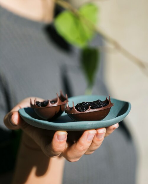 Main de femme tenant des bols à dessert savoureux dans une assiette en céramique