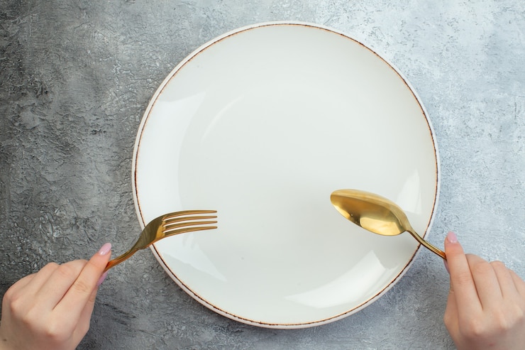 Photo gratuit main de femme tenant des couverts sur une assiette vide sur une surface grise