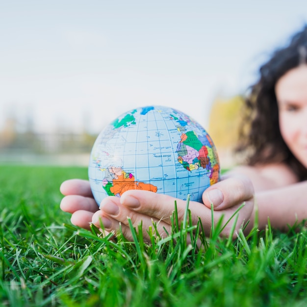 Main de femme tenant le globe sur l&#39;herbe verte