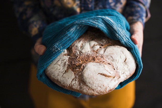 Main de femme tenant un grand pain fraîchement cuit, couvert d&#39;une serviette bleue