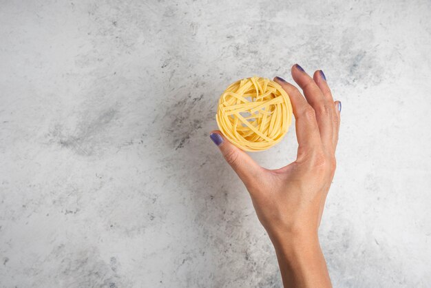 Main de femme tenant le nid de pâtes crues sur fond blanc.