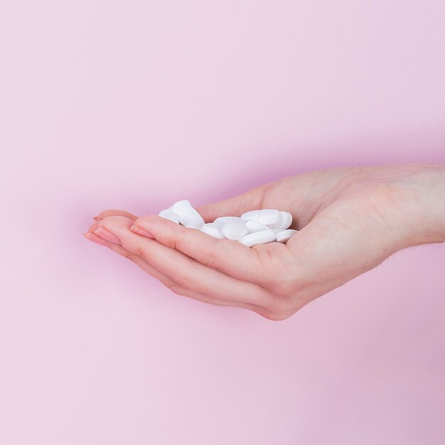 Main de femme tenant des pilules blanches de médecine pharmaceutique
