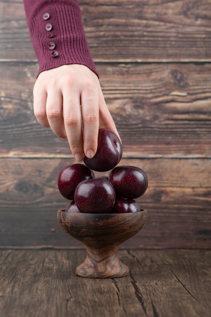 Main De Femme Tenant Une Prune Violette Dans Un Bol En Bois.