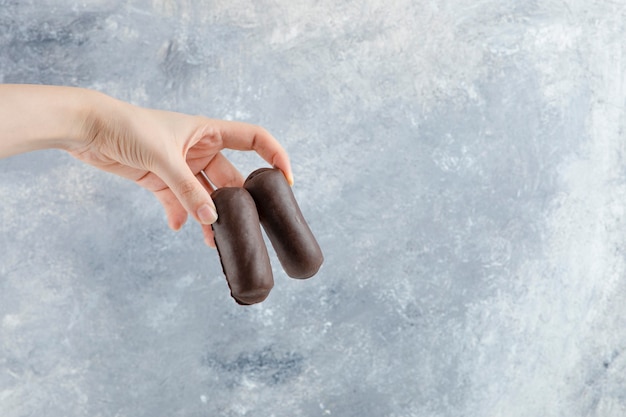 Main de femme tenant le rouleau de crème au chocolat avec de la crème de lait isolé sur fond de marbre.