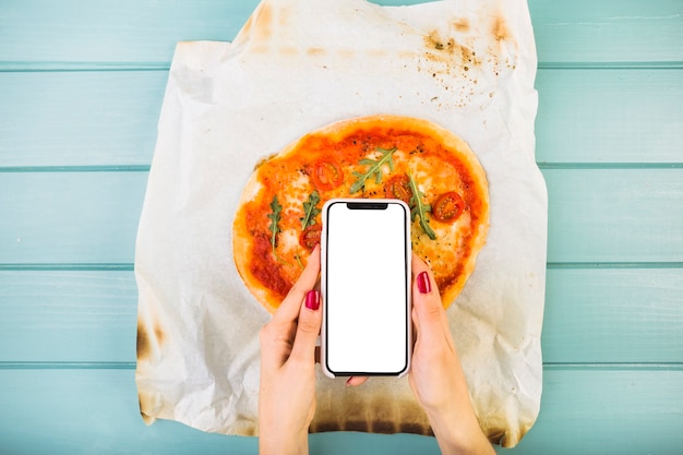 Photo gratuite main de femme tenant le smartphone sur la pizza