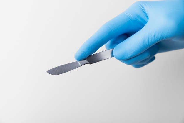 Main avec un gant en caoutchouc tenant un scalpel médical