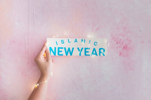 Photo gratuite main avec guirlande tenant le papier de nouvel an islamique