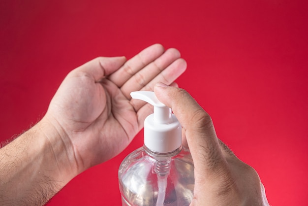 Main de l'homme dans un récipient avec du gel d'alcool sur le rouge