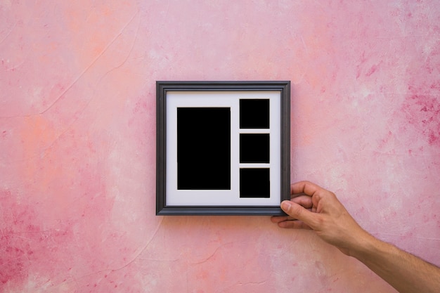 Main de l&#39;homme plaçant le cadre photo sur un mur rose peint