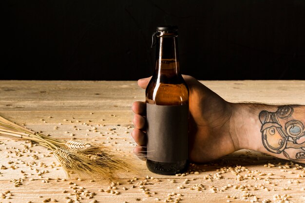 Main de l&#39;homme tenant une bouteille d&#39;alcool avec des épis de blé sur une surface en bois