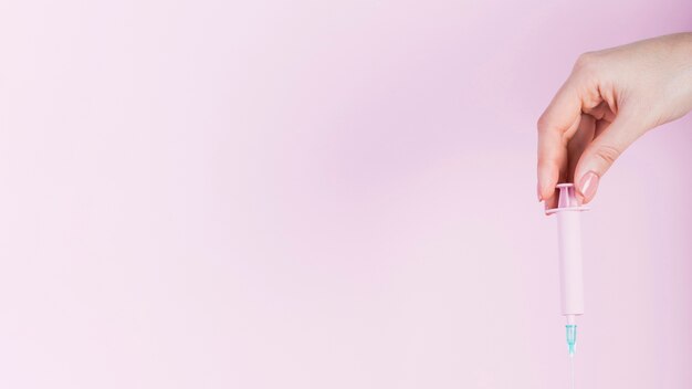 Main de l&#39;homme tenant une seringue en plastique sur fond rose