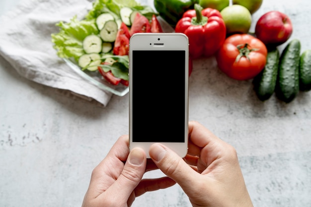 Photo gratuite main de l'homme tenant un téléphone portable sur des légumes biologiques sur fond de béton