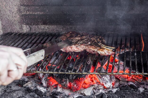 Main humaine rôtir la viande dans la grille du barbecue
