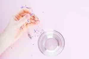 Photo gratuite main humaine tenant une capsule transparente remplie de confettis en plus du verre sur l'eau