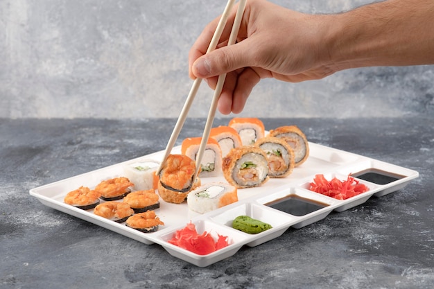 Main masculine prenant le rouleau de sushi avec des baguettes de la plaque blanche