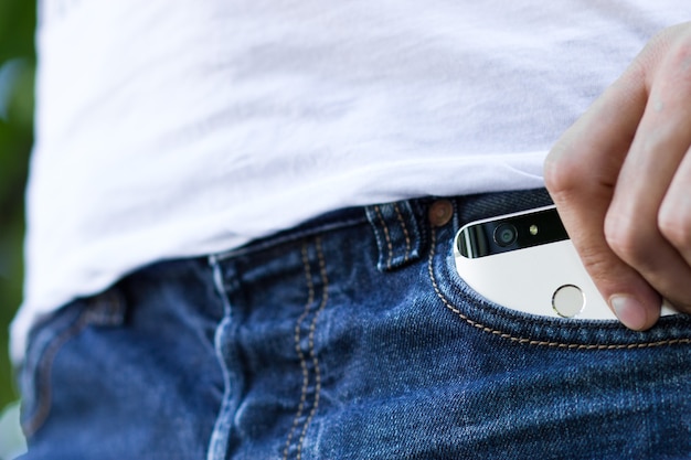 Main masculine saisissant un smartphone dans la poche arrière gauche d'un pantalon jeans