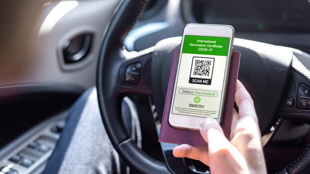 Main masculine tenant un passeport et un smartphone avec certificat de vaccination international Code QR COVID-19 dans une voiture