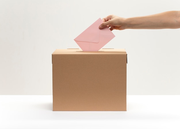 Une main met une enveloppe rose dans la boîte de vote