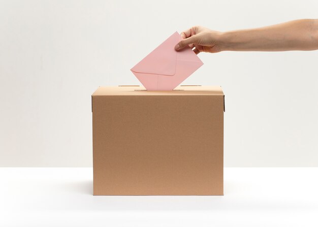 Une main met une enveloppe rose dans la boîte de vote